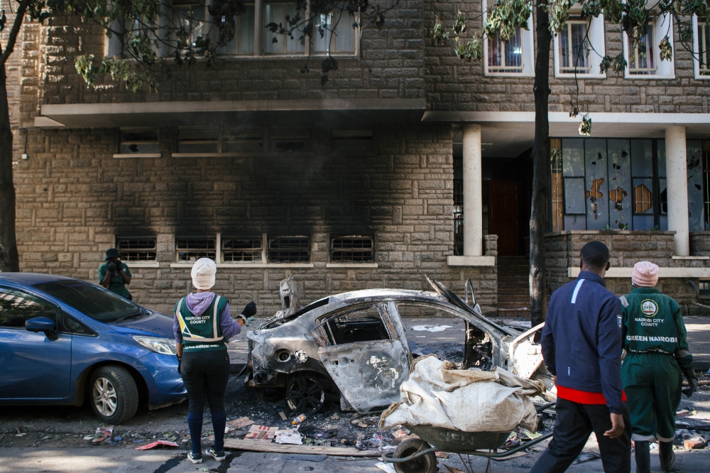 City cleaners look at a burnt-out vehicle following anti-government protests in Nairobi. (Photo by Kang-Chun Cheng/Bloomberg)