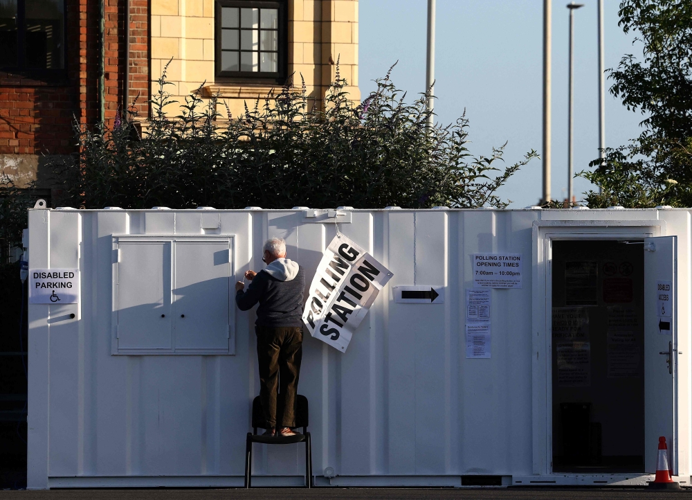 A man hangs a polling station sign on a mobile unit at a Lidl supermarket car park in Loughborough, central England, on July 4, 2024 as Britain holds a general election. (Photo by Darren Staples / AFP)
