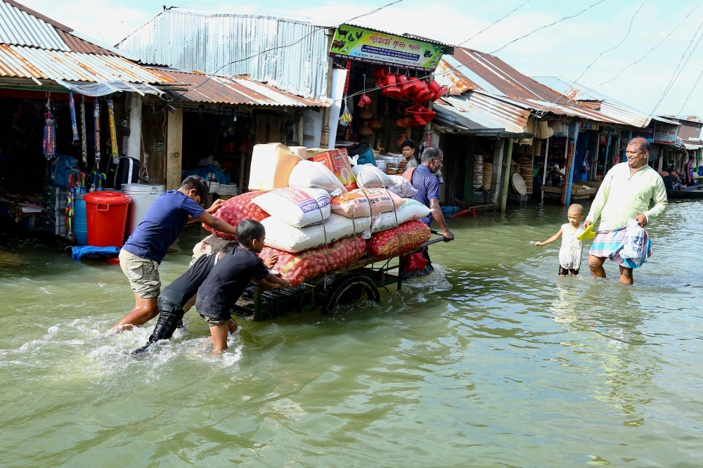 People push a handcart carrying supplies through the flood at Fenchuganj in Sylhet on July 3, 2024. (Photo by Mamun Hossain / AFP)
