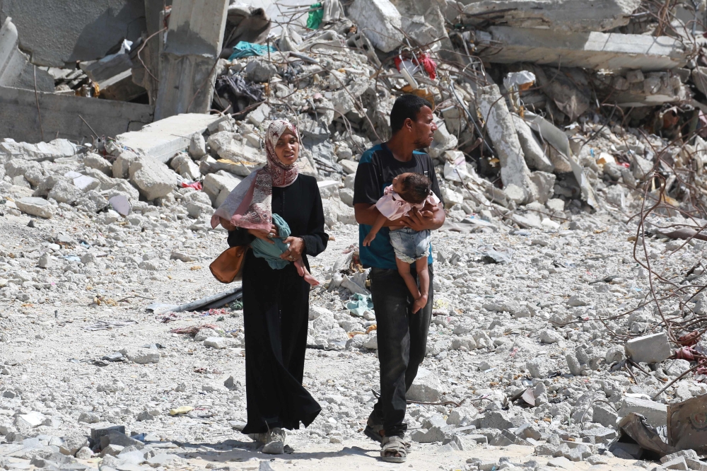 A Palestinian couple holds their children as they walk through debris in Khan Yunis in the southern Gaza Strip on July 4, 2024. (Photo by Bashar TALEB / AFP)

