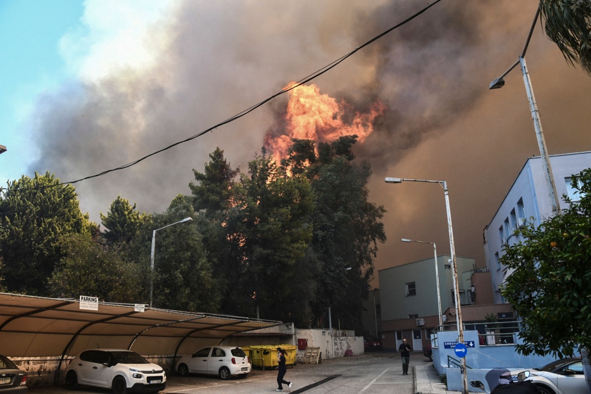 Bystanders flee as a wildfire burns next to a hospital near Patras on July 9, 2024.  (Photo by Eurokinissi / AFP) 
