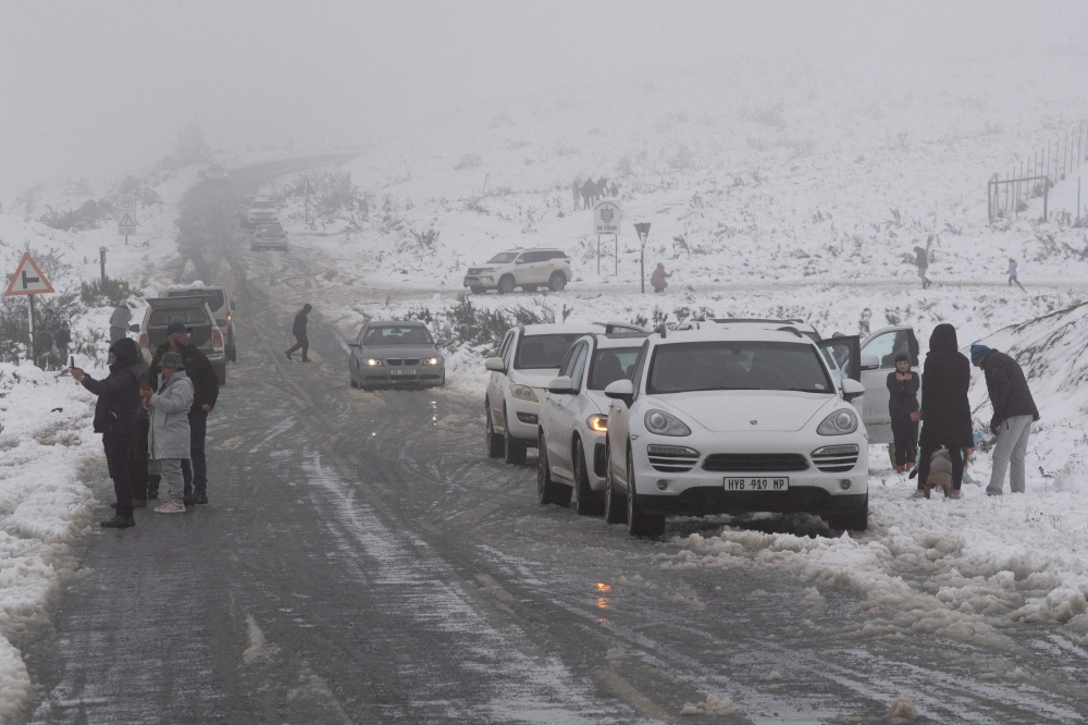 People stand next to a road taking pictures of the unusually heavy snowfall on the mountains around the Bo-Swaarmoed Pass near Ceres on July 8, 2024. (Photo by RODGER BOSCH / AFP)
