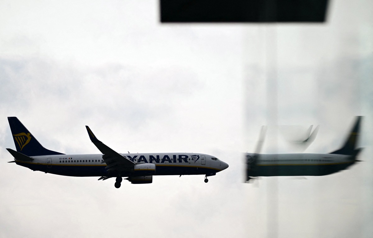 File photo of a Ryanair Boeing 737-8AS aircraft is reflected in a window as it prepares to land at London Gatwick Airport, near Crawley, southern England, on September 26, 2023. (Photo by Ben Stansall / AFP)
