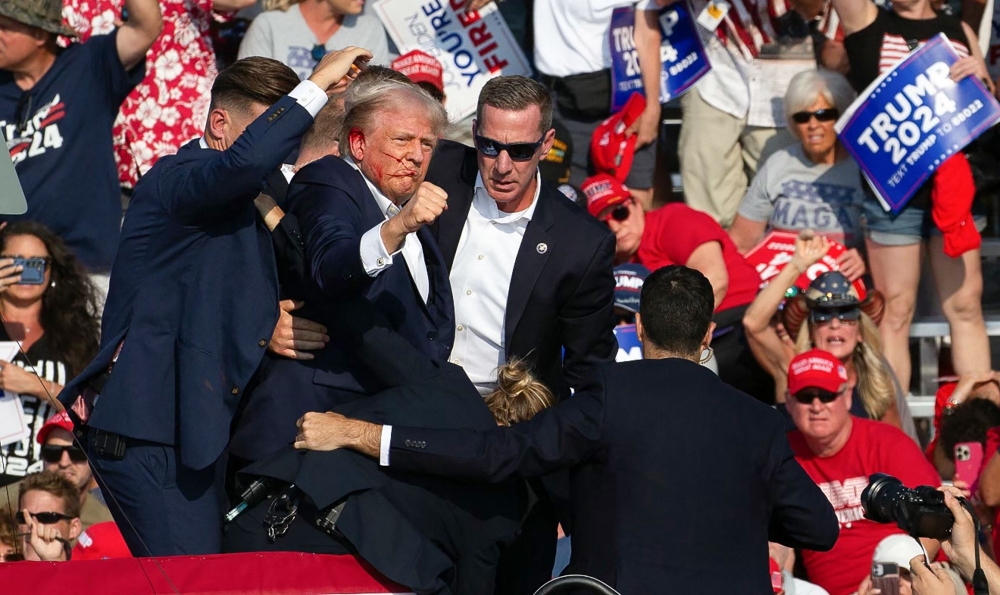 Republican candidate Donald Trump is seen with blood on his face surrounded by secret service agents as he is taken off the stage. (Photo by Rebecca Droke / AFP)