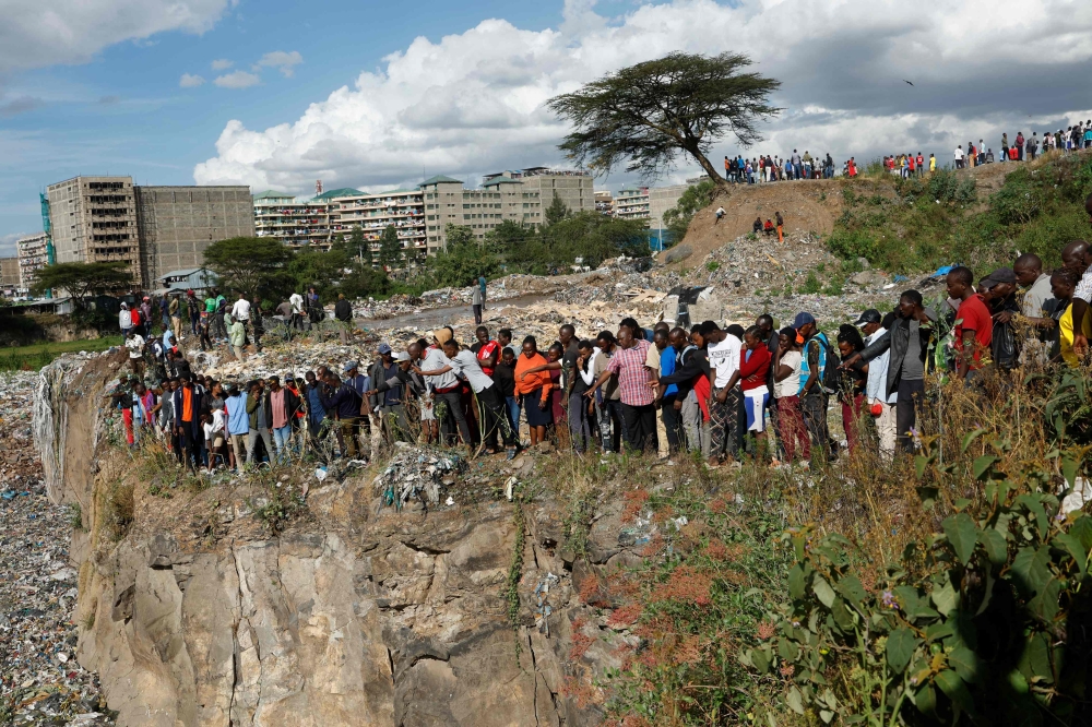 People stand on the edge of a dumpsite in Mukuru slum, Nairobi, on July 12, 2024. (Photo by Simon Maina / AFP) 