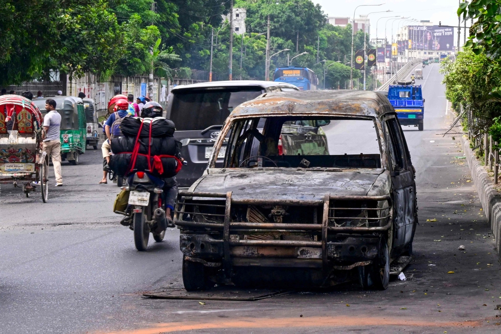 Commuters drive past a burnt car after students set it on fire amid the ongoing anti-quota protest in Dhaka on July 19, 2024. (Photo by Munir UZ ZAMAN / AFP)
