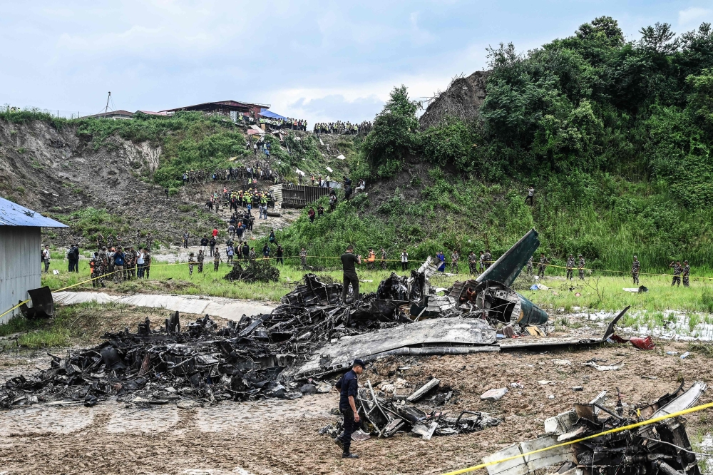 Rescuers and officials stand at the crash site after a Saurya Airlines' plane crashed during takeoff at the Tribhuvan International Airport in Kathmandu on July 24, 2024.  (Photo by Prakash Mathema / AFP)