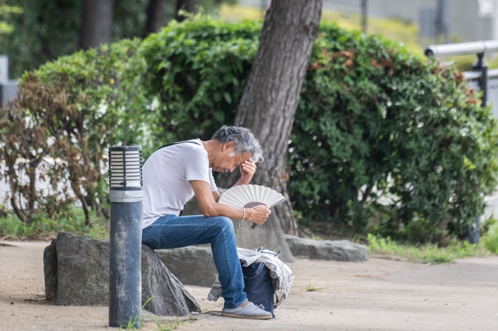 A man uses a folding fan at the Odaiba Seaside Park in Tokyo on July 26, 2024. (Photo by Yuichi Yamazaki / AFP)