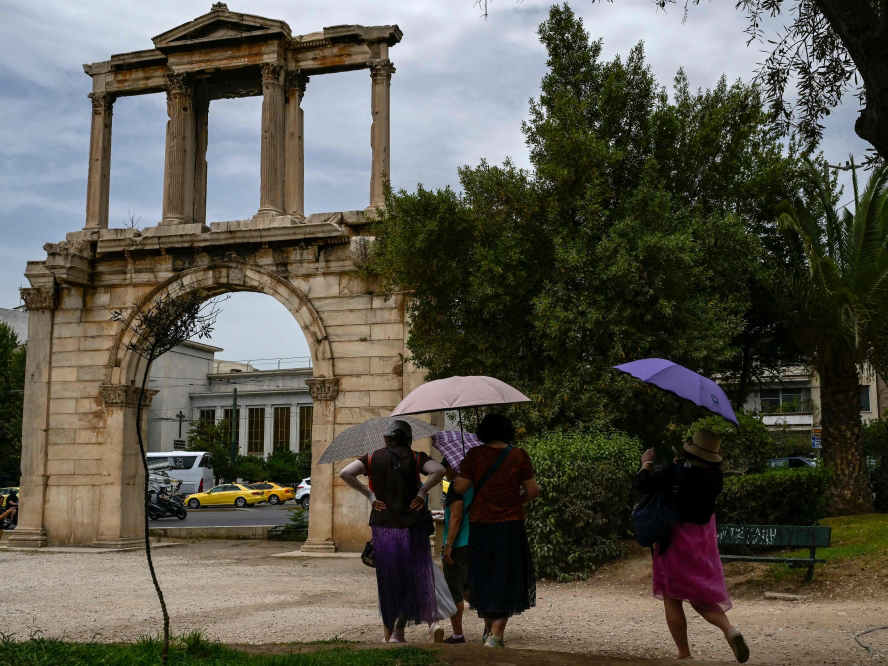 File: Tourists holding umbrellas walk in front of the ancient Roman Andrian Gate, during a hot day in Athens on June 13, 2024. (Photo by Aris Messinis / AFP)

