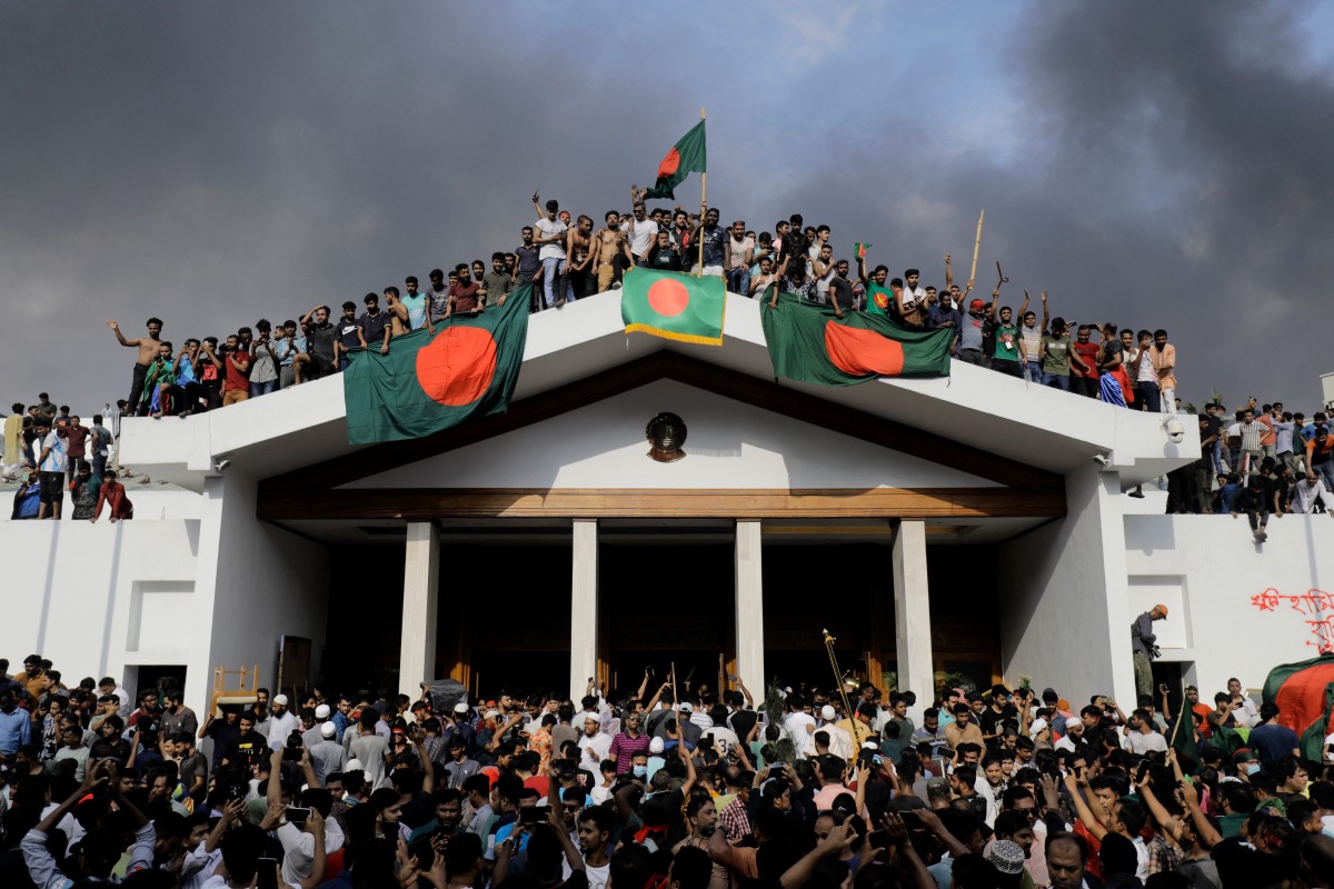 Anti-government protestors display Bangladesh's national flag as they storm Prime Minister Sheikh Hasina's palace in Dhaka on August 5, 2024. Bangladesh army chief Waker-Uz-Zaman spent nearly four decades rising to the top of the military and said on August 5, he was 