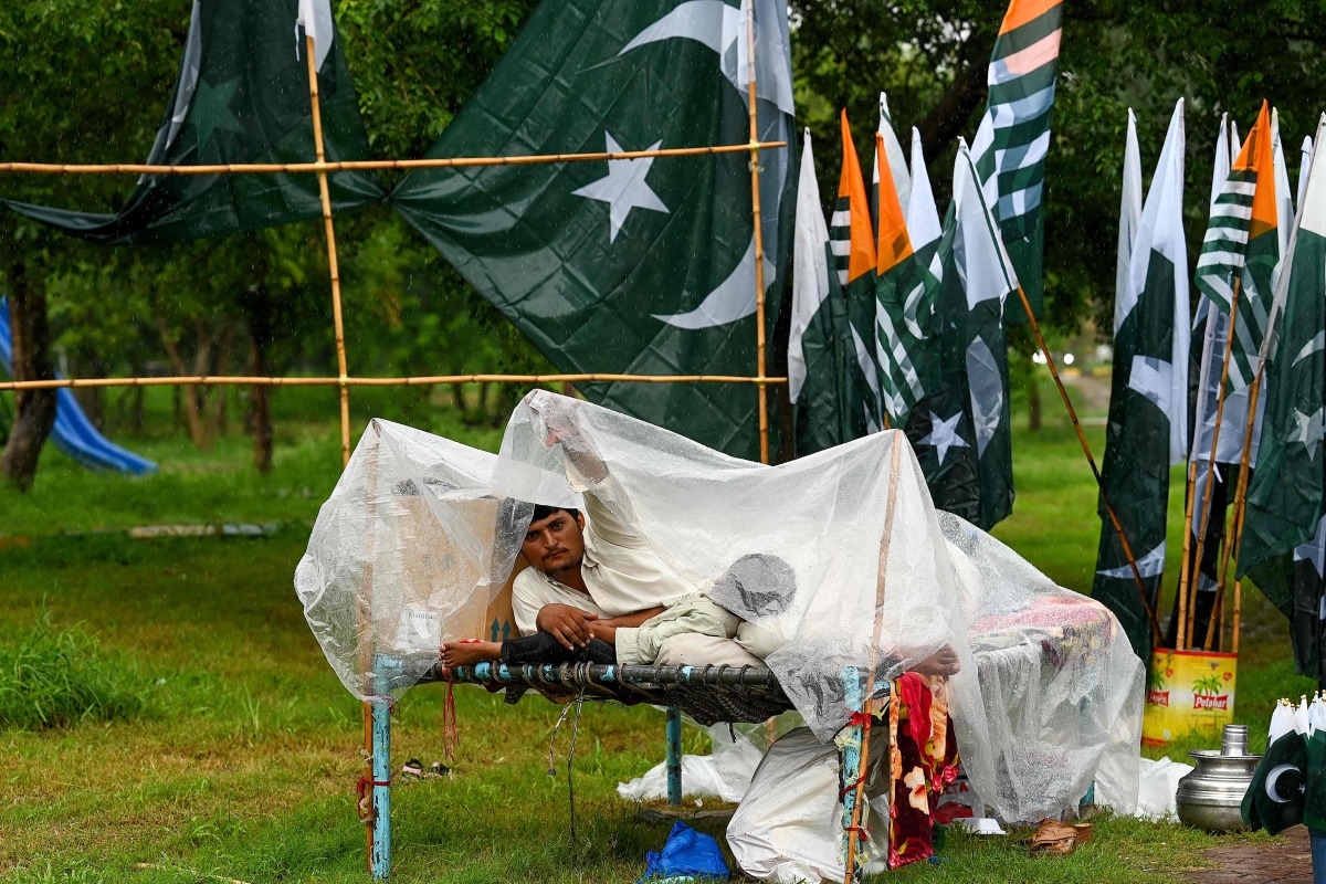 A vendor looks on as he sells PAKISTAN national flags along a street, amid rainfall in Islamabad on August 7, 2024, ahead of the country's independence day. (Photo by Aamir QURESHI / AFP)