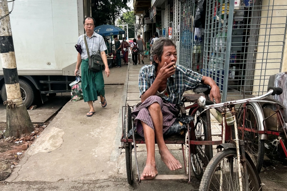 A trishaw driver smokes as he waits for passengers in Yangon on August 13, 2024. (Photo by Saiaung Main / AFP)
