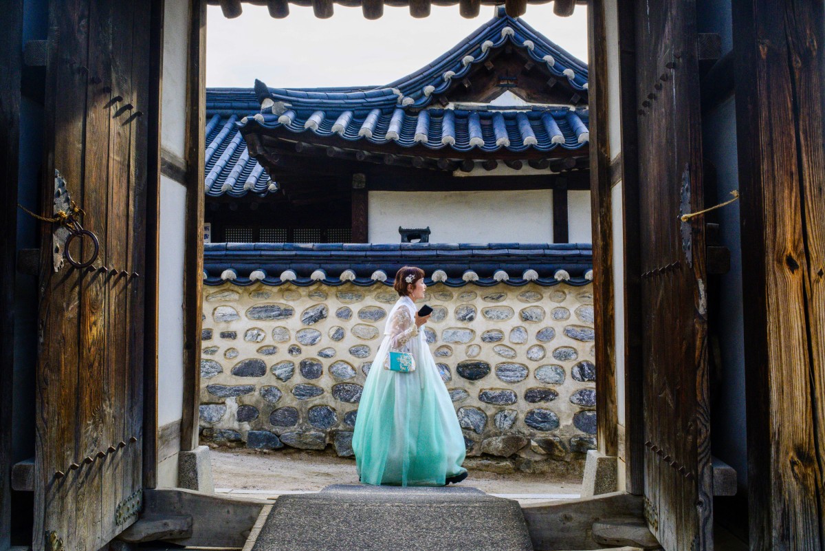 A woman wearing a traditional dress walks past a doorway at Namsangol Hanok Village in Seoul on August 8, 2024. (Photo by ANTHONY WALLACE / AFP)
