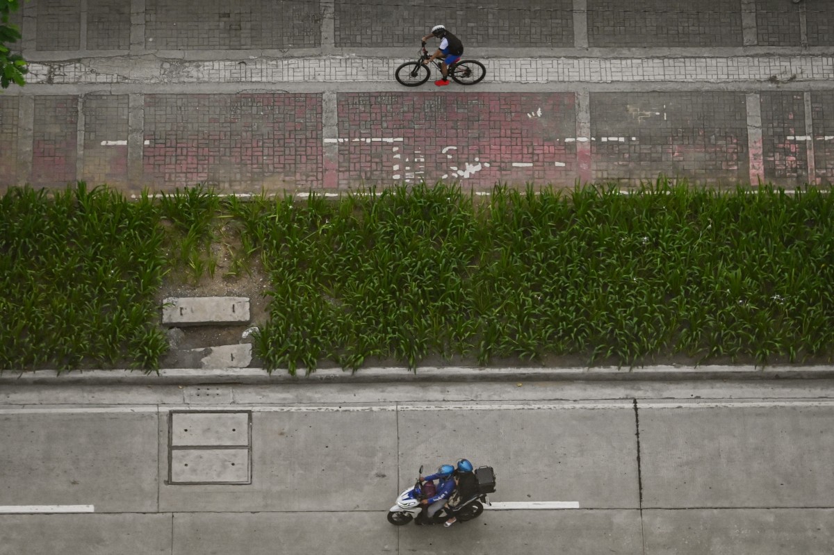 A bicycle (top) and a motorcyle pass by Manila Bay in Manila on August 16, 2024. (Photo by JAM STA ROSA / AFP)
