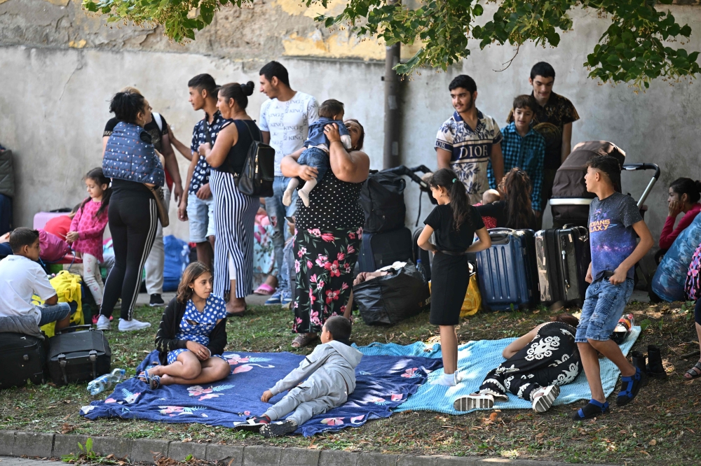 Refugees sit on the pavement close to their former shelter in Kocs village, about 70 km north-west from the Hungarian capital Budapest, on August 21, 2024. (Photo by Attila 
Kisbenedek / AFP)
 