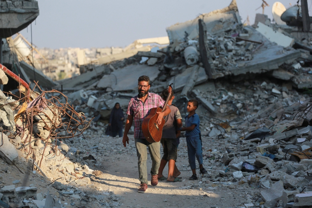  Ahmad Abu Amsha, 42, a music teacher who had to flee Beit Hanun in the northern Gaza Strip, walks in a war-devastated area in Khan Yunis on his way to entertain displaced Palestinian children by playing songs on his guitar on September 1, 2024. (Photo by Bashar TALEB / AFP)
