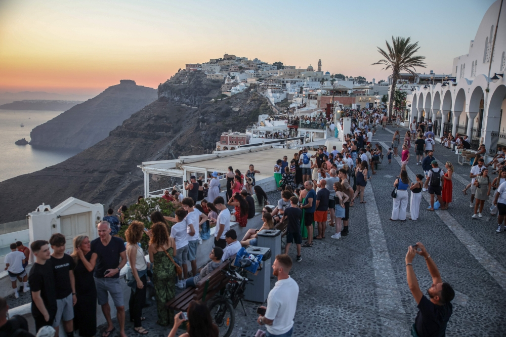 Tourists take pictures of the sunset in the village of Fira on the Greek island of Santorini on July 19, 2024. Photo by Aris Oikonomou / AFP