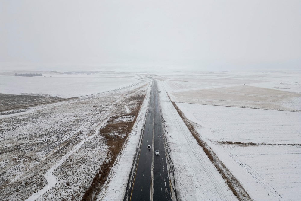 This aerial view taken on September 21, 2024, shows cars driving on a road next to snowfall on farmlands near Warden, Free State province, South Africa. (Photo by Wikus de Wet / AFP)