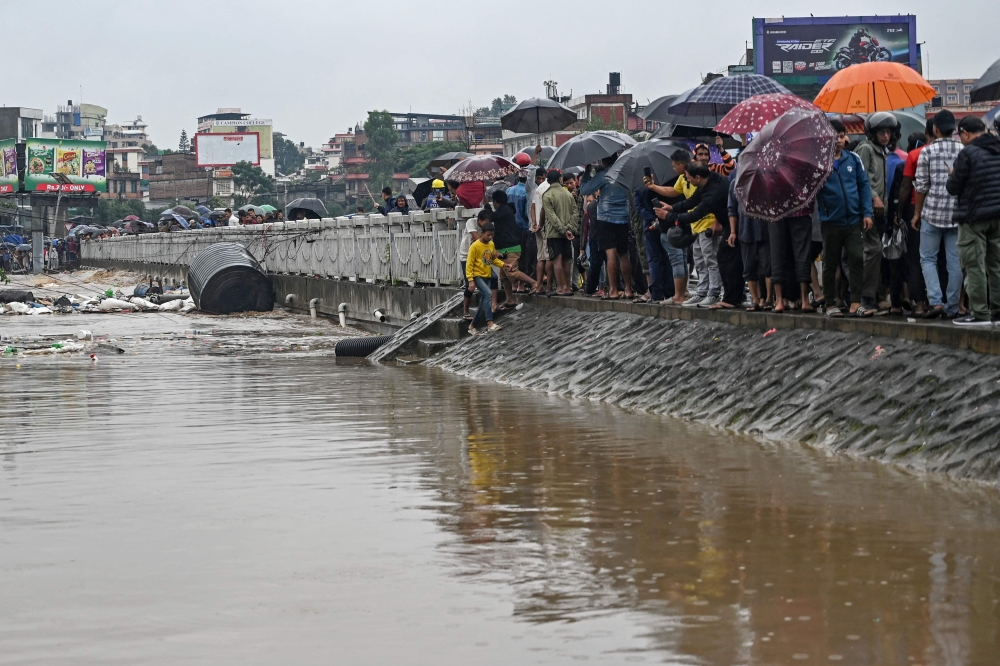 Residents stand along a street as they inspect flood waters after the Bagmati river overflowed during monsoon rains in Kathmandu on September 28, 2024. (Photo by Prakash Mathema / AFP)
 