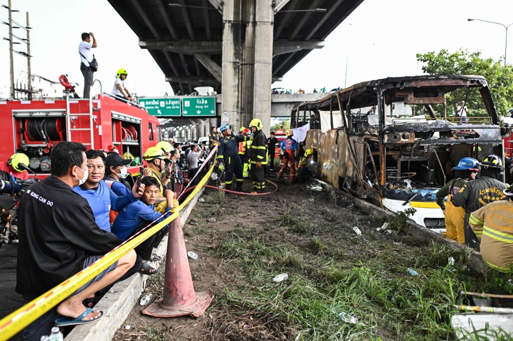 Firefighters and rescue workers stand next to a burnt-out bus that was carrying students and teachers on the outskirts of Bangkok, on October 1, 2024. (Photo by Manan VATSYAYANA / AFP)
