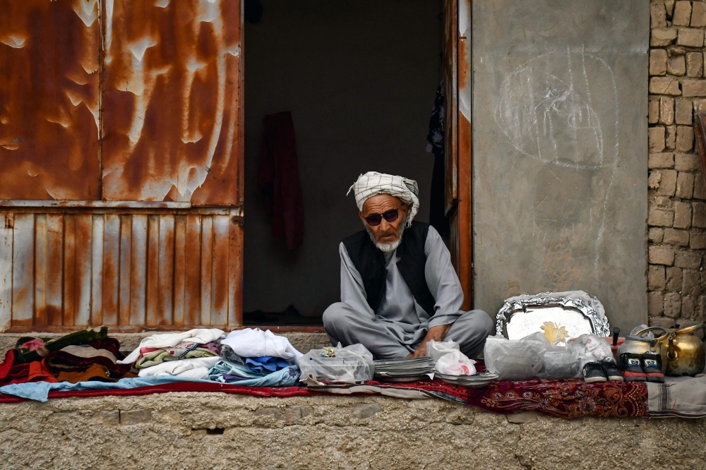 An Afghan vendor selling clothes waits for customers along a street on the outskirts of Mazar-i-Sharif on October 6, 2024. (Photo by Atif Aryan / AFP)
