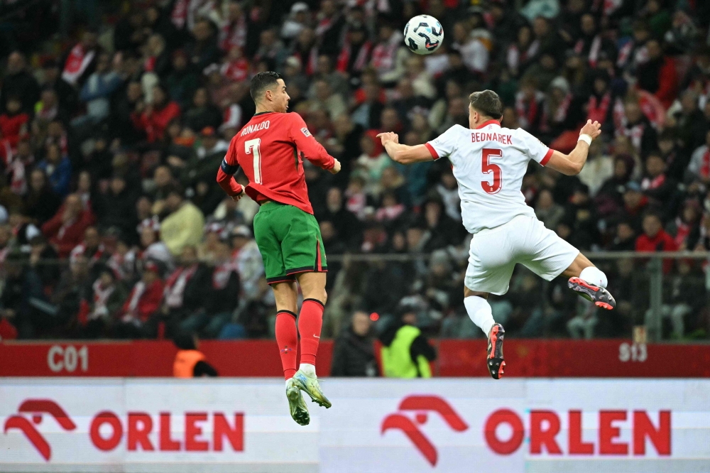 Portugal's forward #07 Cristiano Ronaldo and Poland's defender #05 Jan Bednarek both jump to head the ball during the UEFA Nations League in Warsaw, Poland on October 12, 2024. (Photo by Sergei Gapon / AFP)
 