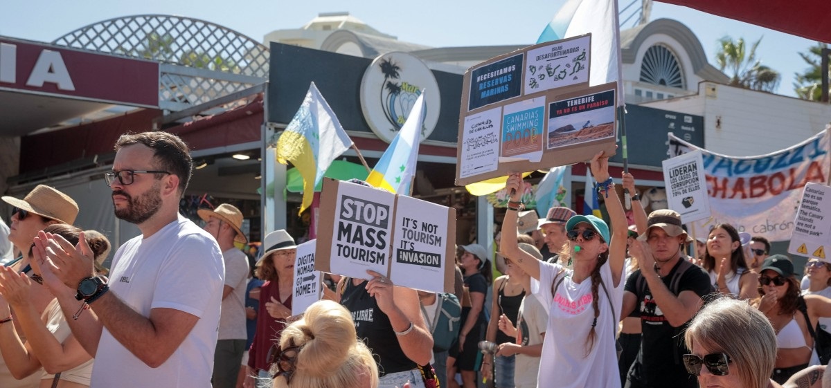 Protesters march during demonstration against mass tourism as tourists sit in a terrace, in Arona on the Spanish Canary island of Tenerife, on October 20, 2024. Photo by DESIREE MARTIN / AFP.
