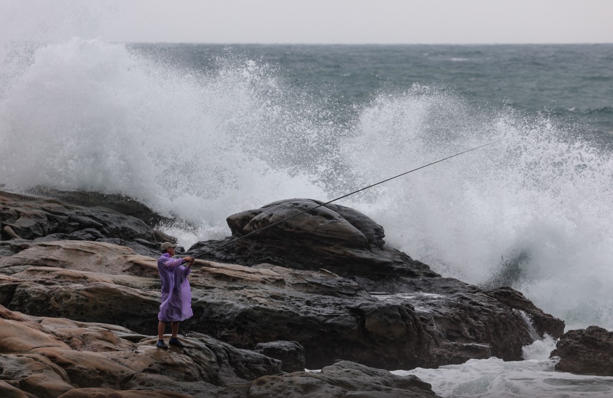 A fisherman holds a fishing rod next to waves as Typhoon Kong-rey approaches, in Keelung on October 29, 2024. (Photo by I-Hwa CHENG / AFP)