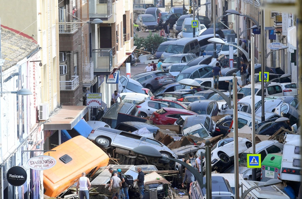 Pedestrians stand next to piled up cars following deadly floods in Sedavi, south of Valencia, eastern Spain, on October 30, 2024. (Photo by Jose Jordan / AFP)