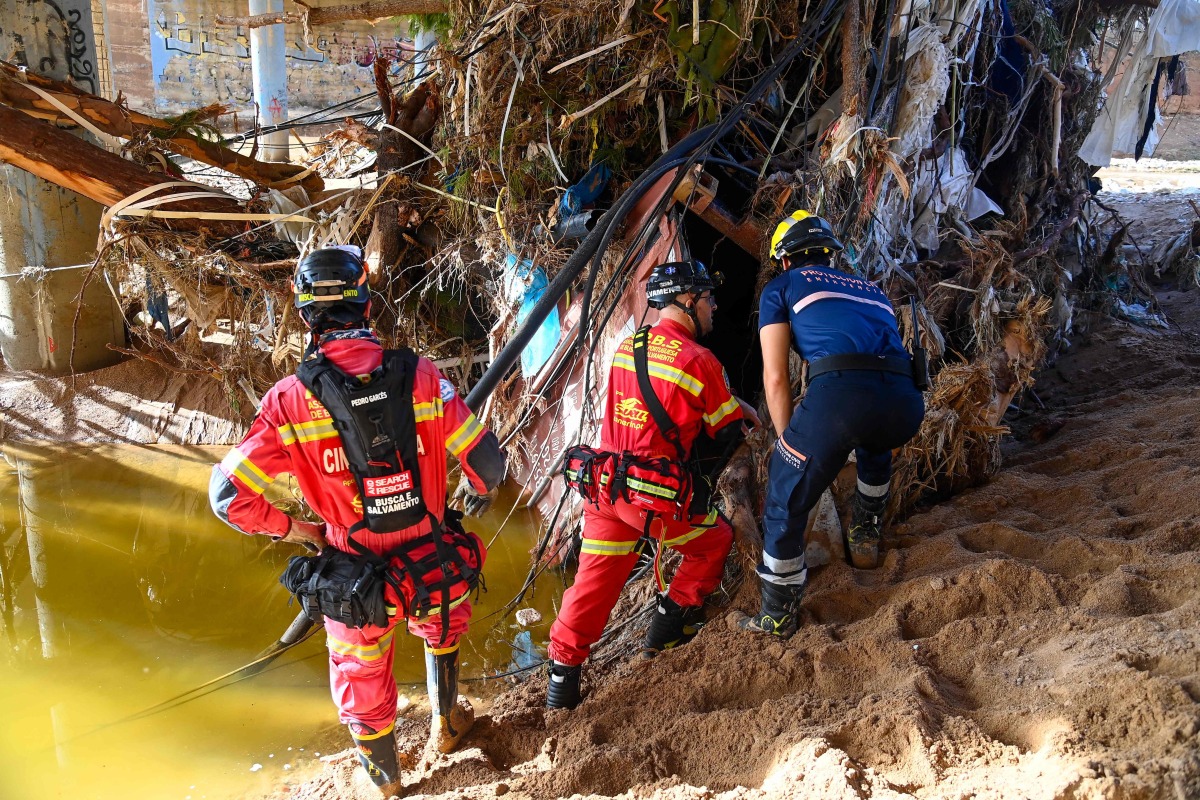 Portuguese firefighters and a civil protection worker search for victims in debris beside a riverbank on November 2, 2024, in the aftermath of devastating floolding in the town of Paiporta, in the region of Valencia, eastern Spain. Photo by JOSE JORDAN / AFP