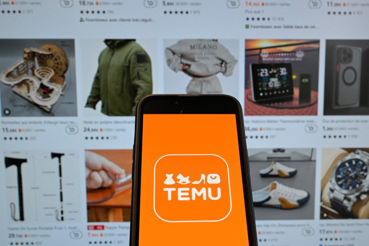 (FILES) This photograph shows the logo of Chinese e-commerce company Temu displayed on a mobile phone in front of a screen showing the company's website in Brussels on November 4, 2024. (Photo by Nicolas TUCAT / AFP)
