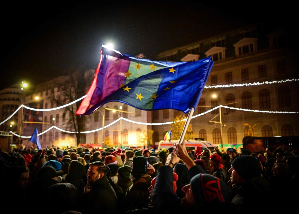 Demonstrators hold EU and Romanian national flags during a pro-European rally and in support of democracy at Piata Universitatii square in Bucharest on December 5, 2024. (Photo by Daniel Mihailescu / AFP)