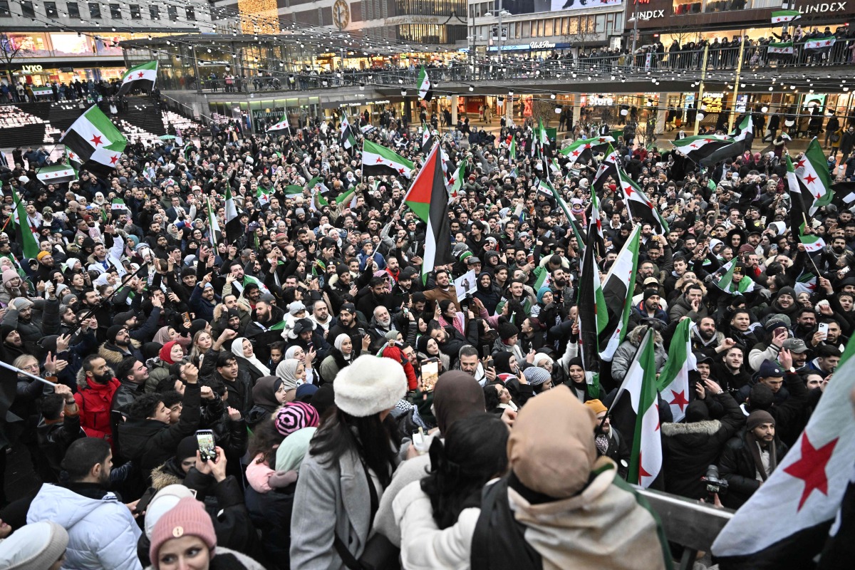 Members of the Syrian community hold Syrian flags as they rally on December 8, 2024 on Sergel's Square in Stockholm, Sweden, to celebrate the end of Syrian dictator Bashar al-Assad's rule after rebel fighters took control of the Syrian capital Damascus overnight. (Photo by Jonas EKSTROMER / TT NEWS AGENCY / AFP) / Sweden OUT
