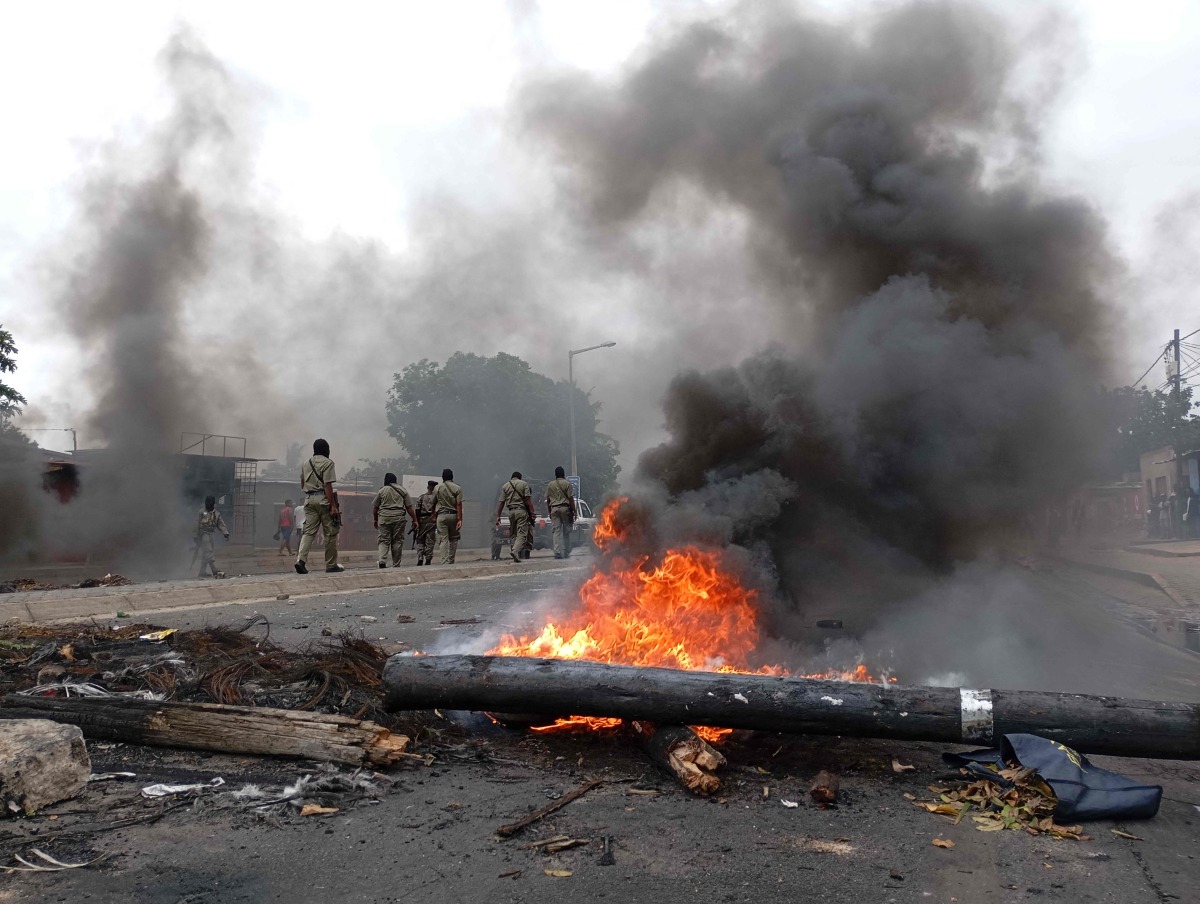 Pedestrians walk past a burning barricade in Maputo on December 24, 2024. (Photo by Amilton Neves / AFP)
