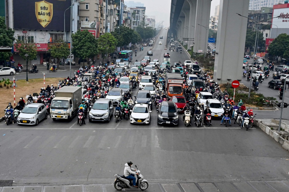 A man rides a motorbike in front of vehicles waiting at a red light at an intersection in Hanoi on January 8, 2025. (Photo by Nhac NGUYEN / AFP)
