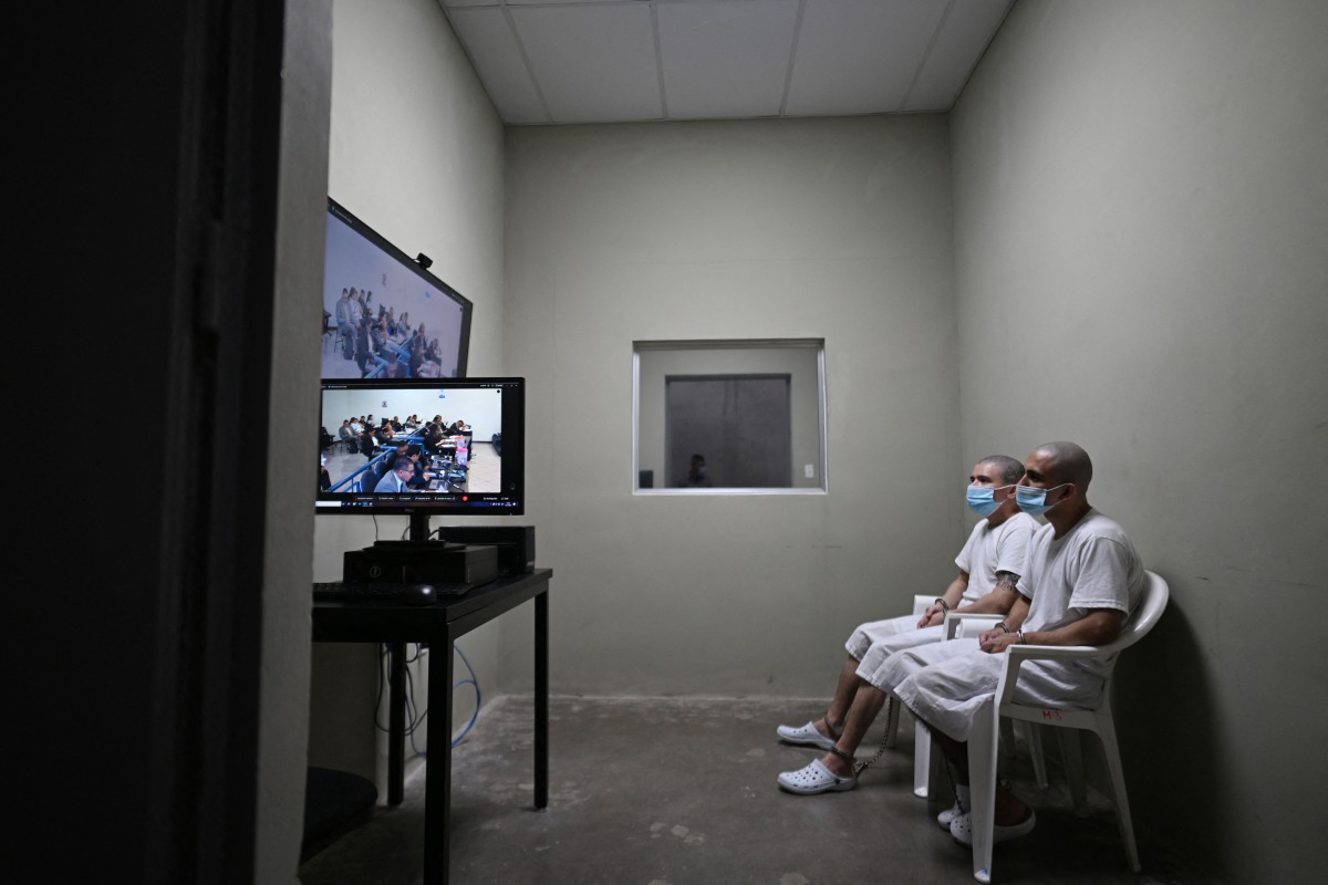 Two inmates watch a virtual trial at the Counter-Terrorism Confinement Centre (CECOT) mega-prison, where hundreds of members of the MS-13 and 18 Street gangs are being held, in Tecoluca, El Salvador on January 27, 2025. (Photo by Marvin RECINOS / AFP)
