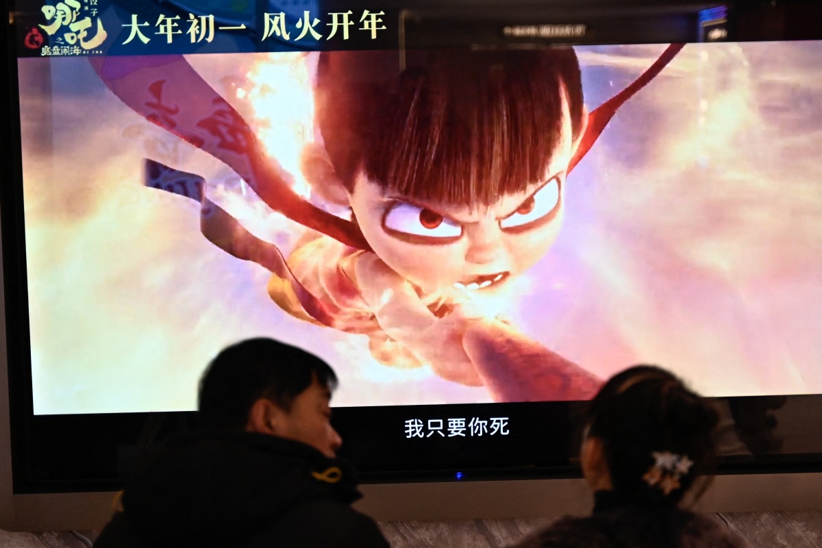 People wait as a screen displays a scene from the Ne Zha 2 animated film at a movie theatre in Beijing on February 16, 2025. (Photo by Pedro PARDO / AFP)
