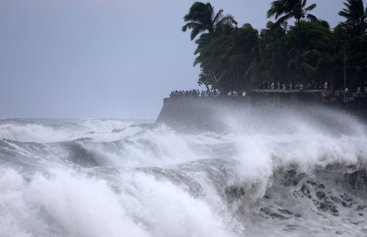 People watch as waves lash against the shore in Saint-Denis de la Reunion, on the French overseas territory island of La Reunion, as the tropical cyclone 