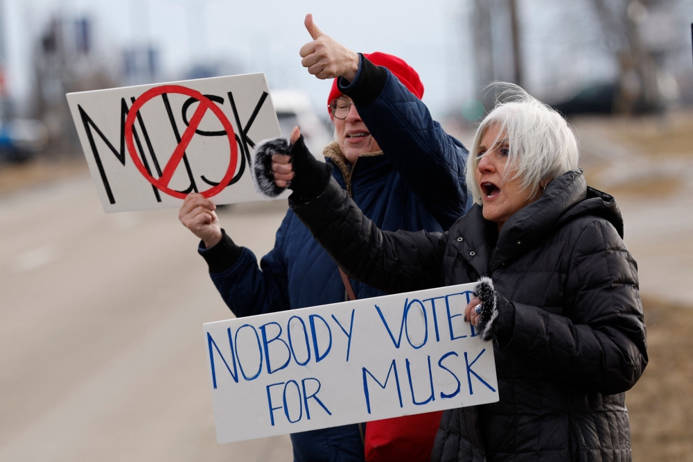 People hold signs during a protest against Elon Musk outside of a Tesla dealership in West Bloomfield, Michigan, on February 27, 2025. (Photo by Jeff Kowalsky / AFP)