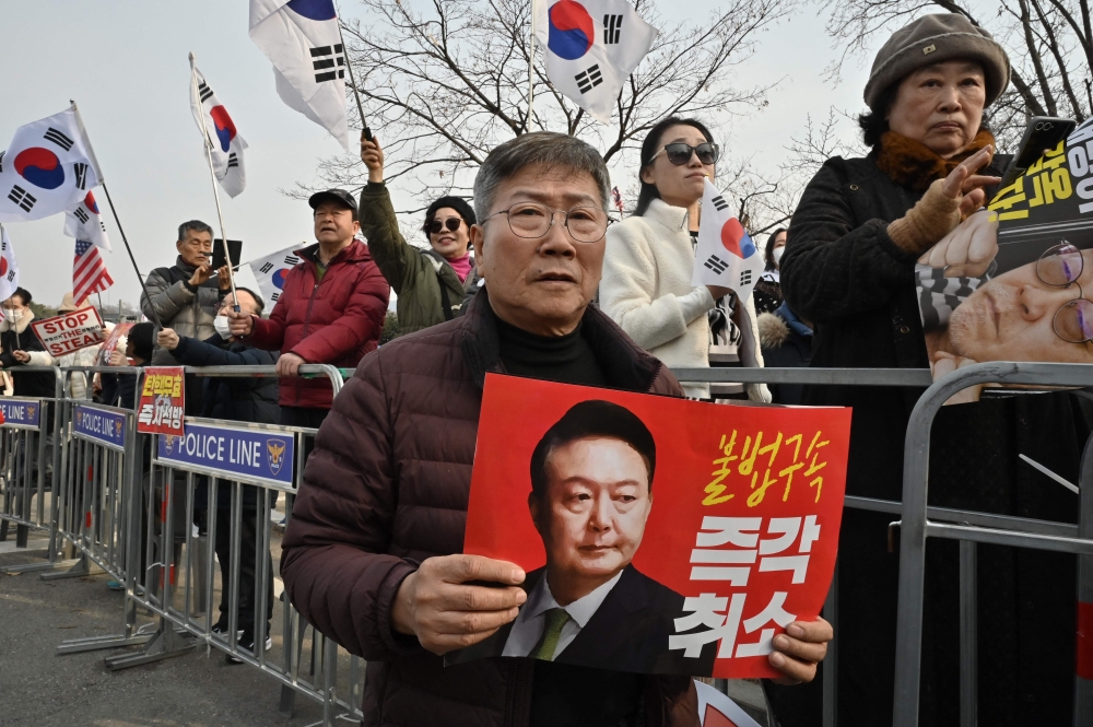 Supporters of arrested and impeached South Korean President Yoon Suk Yeol hold a placard showing a picture of Yoon and reading 