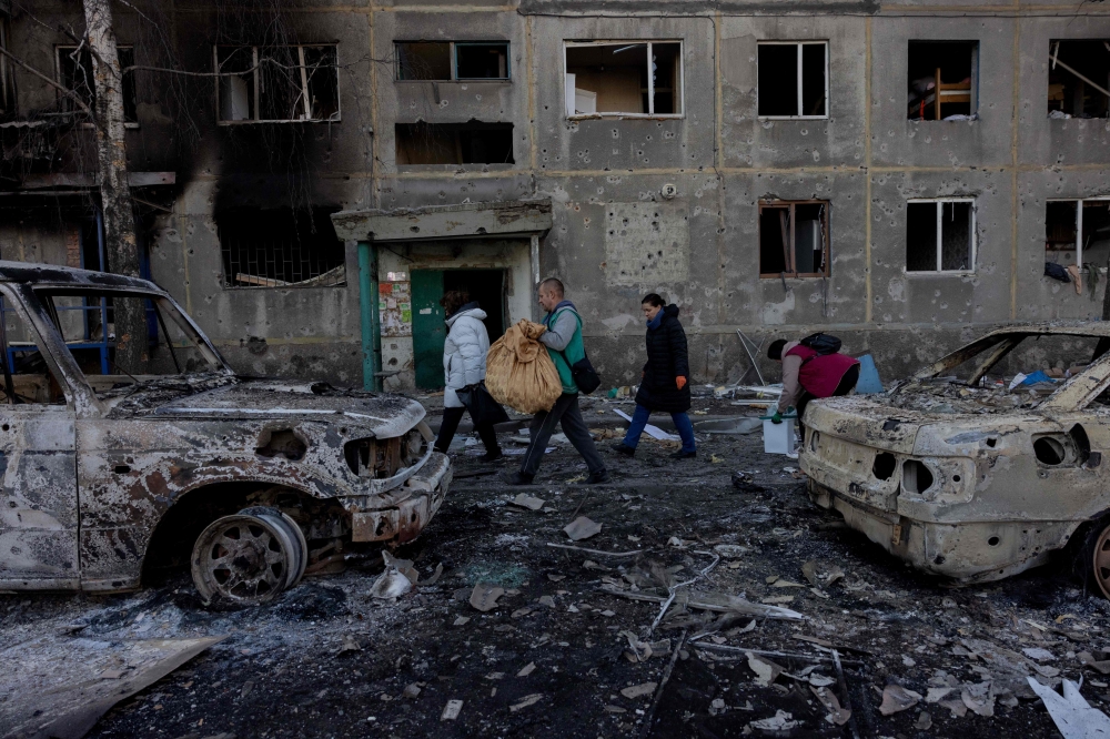 People carry their belongings as they leave their damaged residential building following a strike in Dobropillia, Donetsk region, on March 8, 2025. (Photo by Tetiana DZHAFAROVA / AFP)
