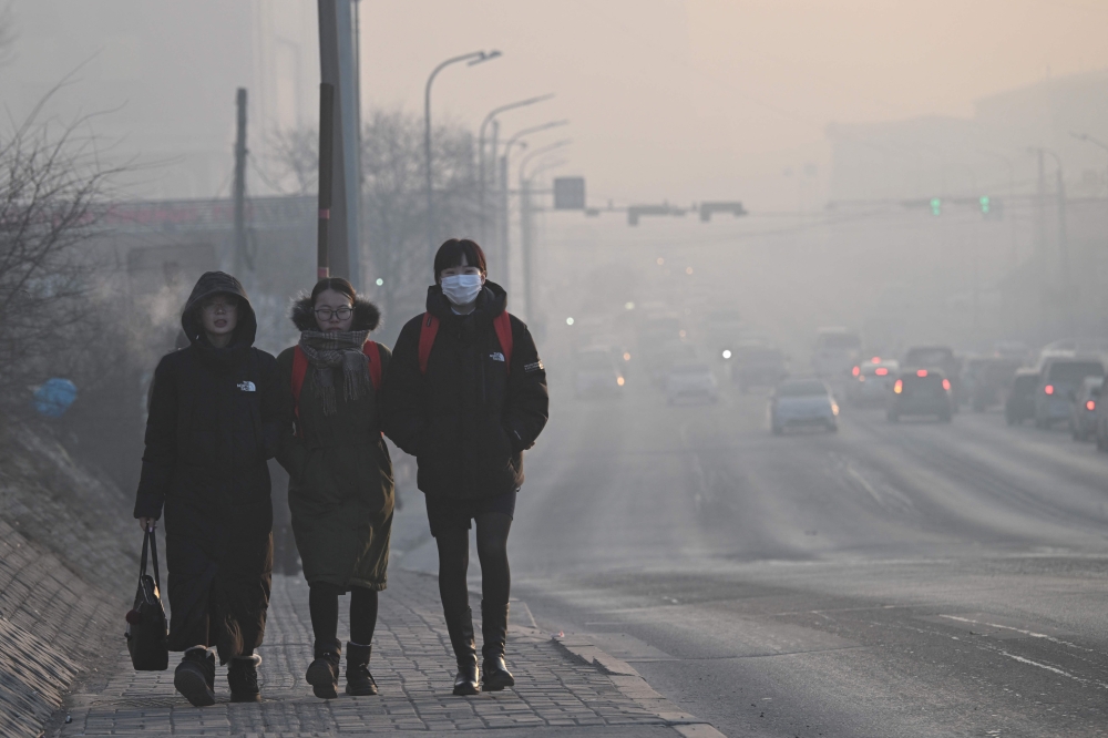 This photo taken on February 18, 2025 shows people walking as motorists commute on a road on a polluted day in Ulaanbaatar, the capital of Mongolia. (Photo by Jade Gao / AFP) 