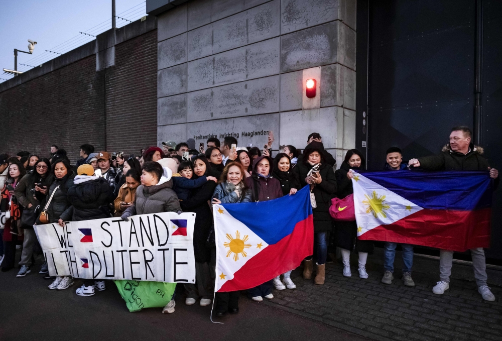 Protesters holding Filipino flags and a banner in support of former Philippine President Rodrigo Duterte gather outside the The Hague Penitentiary Institution prison, which houses the International Criminal Court's (ICC) detention unit, on March 12, 2025. (Photo by Ramon van Flymen / ANP / AFP)
