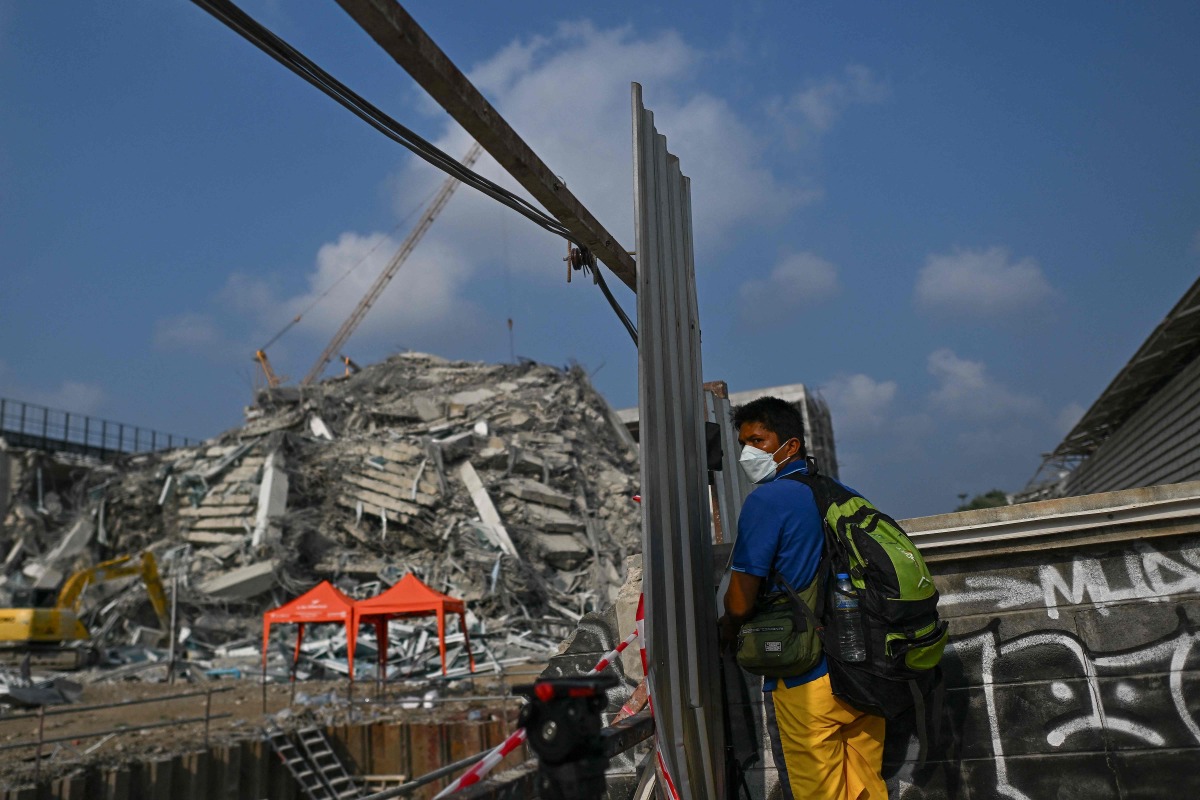 A man uses his smartphone to record at the site of an under-construction building collapse in Bangkok on March 29, 2025, a day after an earthquake struck central Myanmar and Thailand. (Photo by MANAN VATSYAYANA / AFP)