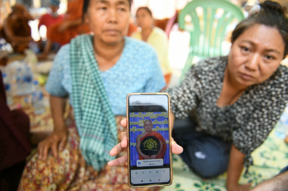 A woman shows a picture of a missing monk during search and rescue operations at a damaged temple in Mandalay on March 30, 2025. (Photo by Sai Aung Main / AFP)