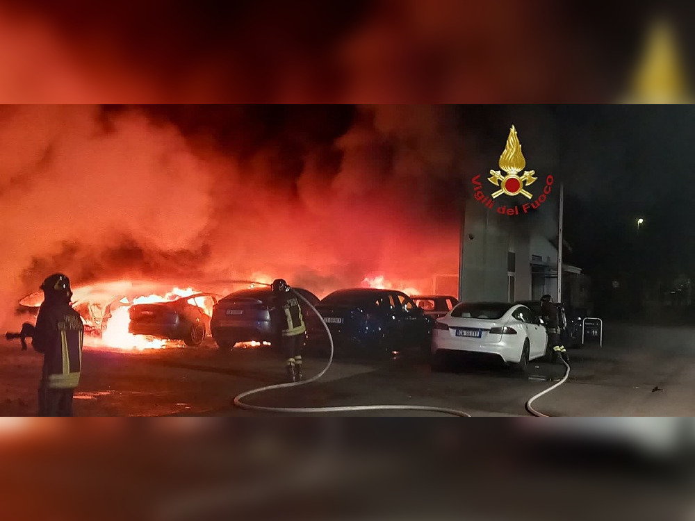This handout image taken and released on March 31, 2025, by the Vigili del Fuoco, the Italian Corps of Firefighters, shows firefighters working to put out a fire at a Tesla dealership, in which 17 cars were destroyed or seriously damaged, in Torrenova, on the outskirts of Rome. (Photo by Handout / Vigili del Fuoco / AFP) 

