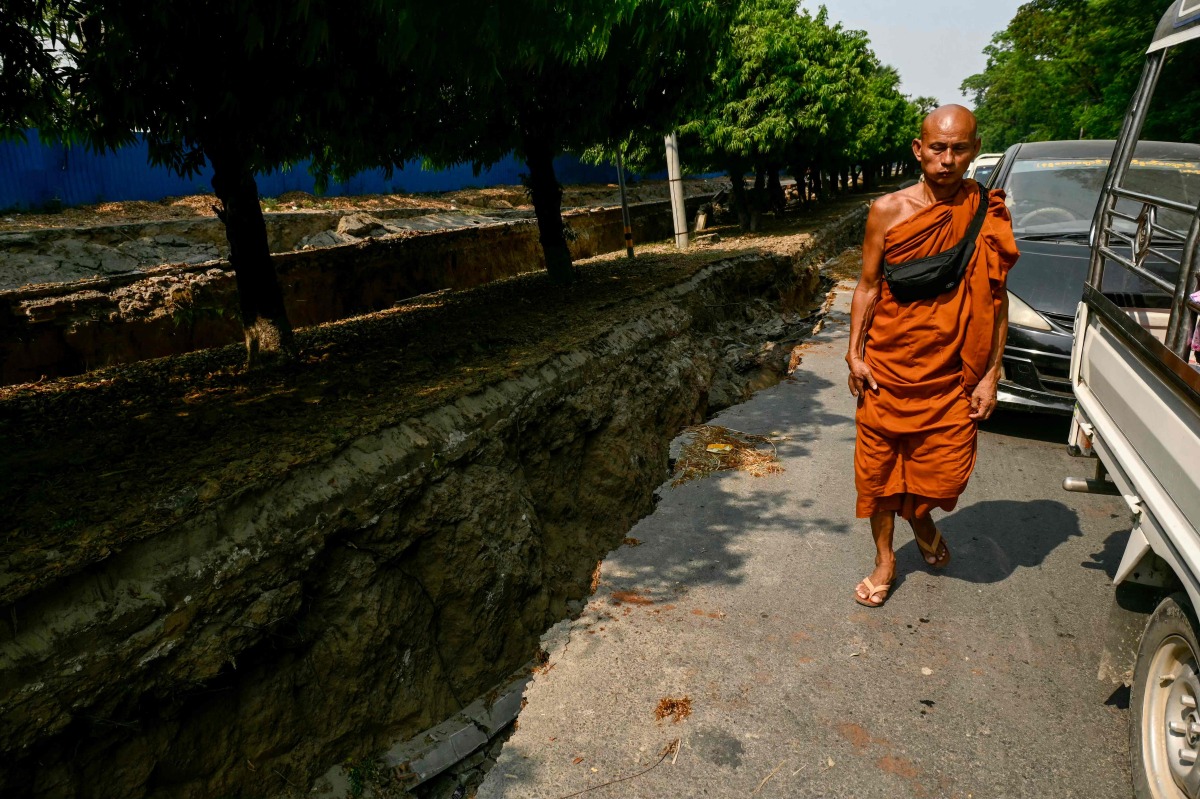 A monk walks past vehicles on the edge of a large crack in the ground along Myo Patt Road linking Mandalay and Sagaing Township on the outskirts of Mandalay on April 2, 2025, five days after a major earthquake struck central Myanmar. Photo by Sai Aung MAIN / AFP