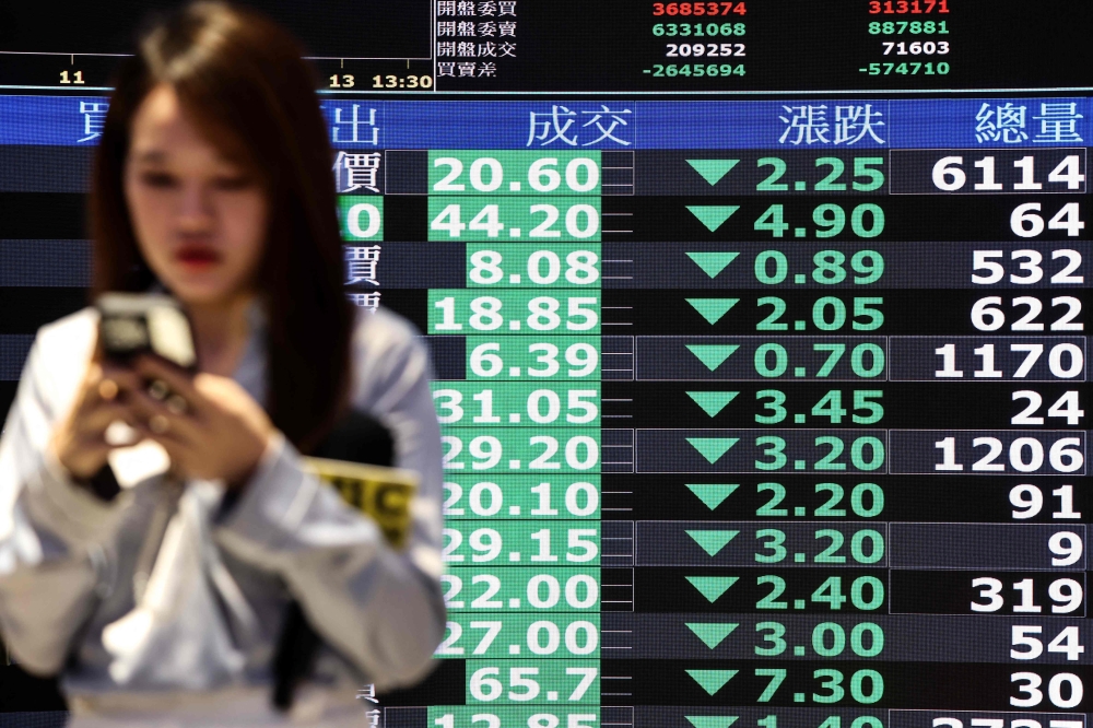A woman walks past screens displaying average stock prices at the Taiwan Stock Exchange in Taipei on April 7, 2025. (Photo by I-Hwa Cheng / AFP)