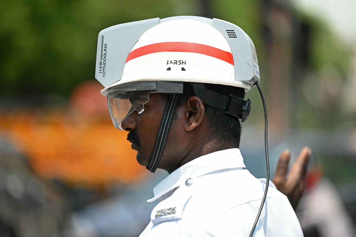 A traffic policeman uses an air-conditioned helmet to get respite from the heat while working at a road junction on a hot summer day in Chennai on April 8, 2025. Photo by R.Satish BABU / AFP
