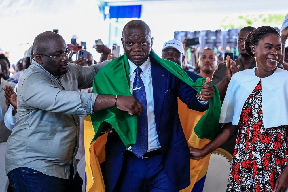 Gabon's junta chief Brice Oligui Nguema is draped with a Gabon flag while standing next to his wife Zita Nyangue Oligui Nguema as they celebrate him winning the presidential election, at his election campaign headquarters in Libreville on April 13, 2025. G(Photo by Daniel Beloumou Olomo / AFP)